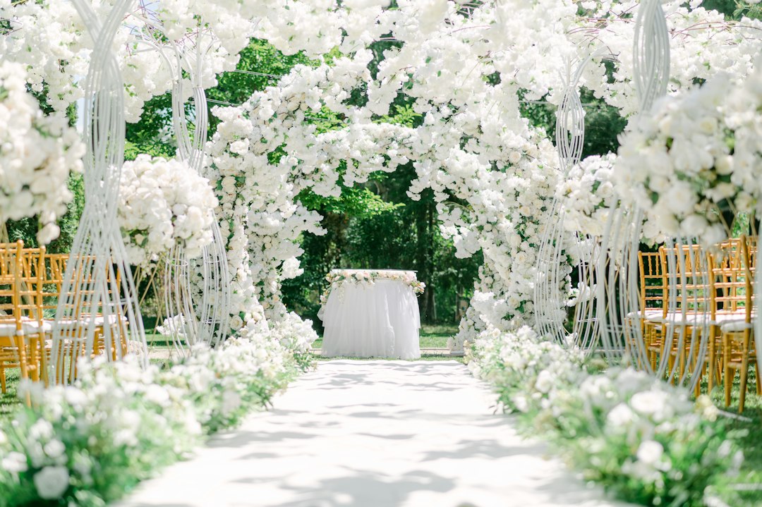 A white floral archway over a path with gold chairs for a wedding